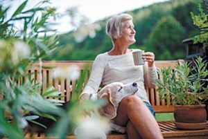 A senior woman with a dog and coffee sitting outdoors on a terrace on sunny day in summer.