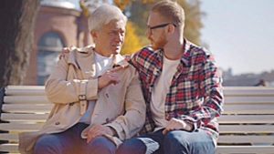 Senior father with adult son talking relaxing on bench in city center